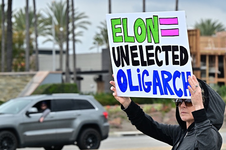 A protester holds up a sign that says, "Elon = unelected oligarch"