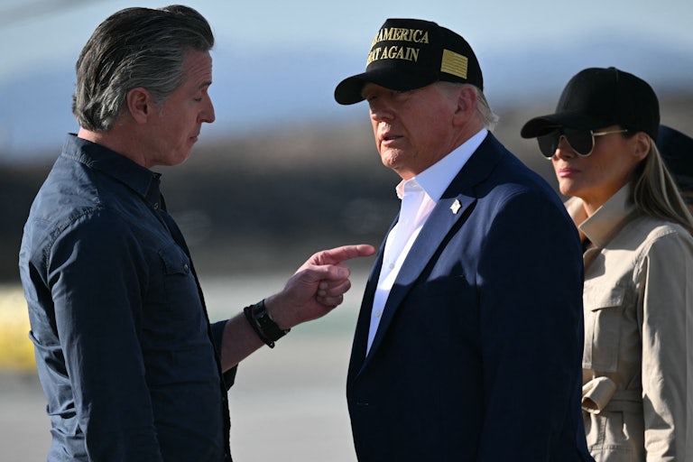 California Governor Gavin Newsom and Donald Trump speak while standing on a tarmac. Melania Trump stands behind her husband.