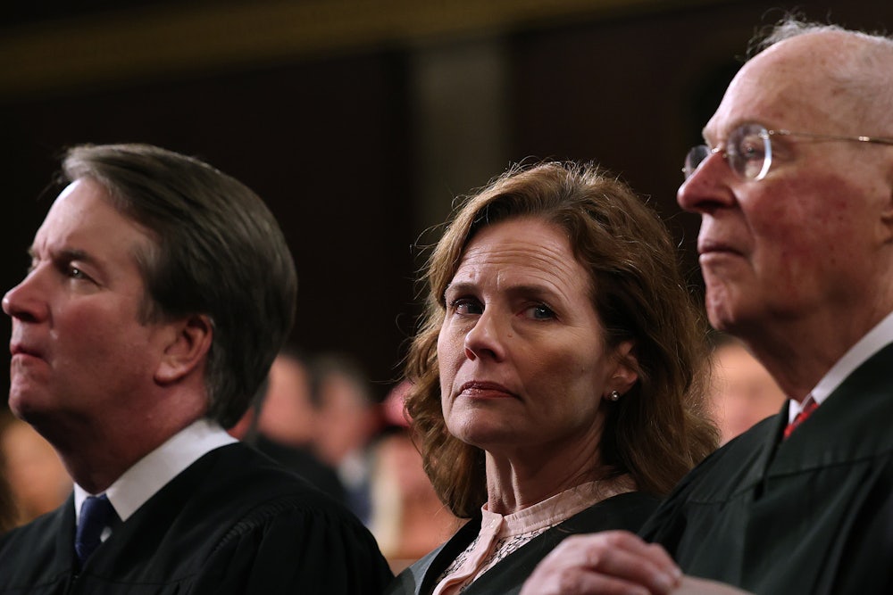 Amy Coney Barrett looks toward the camera, with Kavanaugh and Kennedy on either side of her.