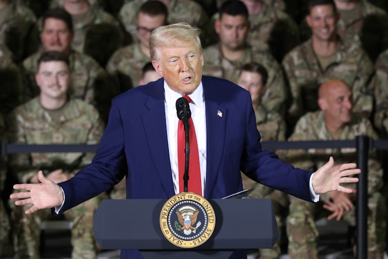 Donald Trump speaks at a lectern in front of many troops.