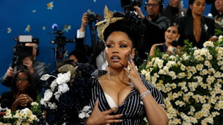 Nicki Minaj poses for the cameras on a red carpet. She rests her super long fingernails on her face and chest.