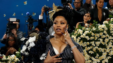 Nicki Minaj poses for the cameras on a red carpet. She rests her super long fingernails on her face and chest.