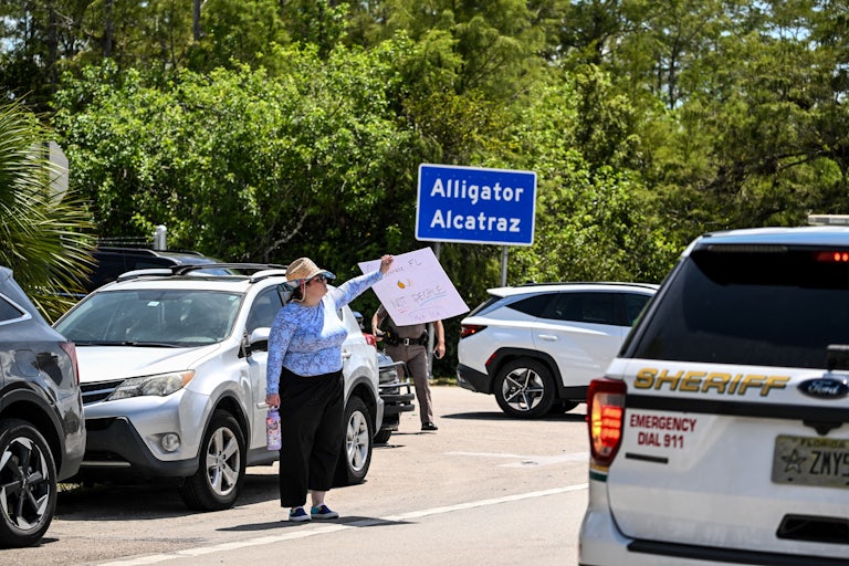Cars are parked by the sign for Alligator Alcatraz as protesters demand its closure