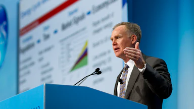Alan Armstrong speaks behind a blue podium with CERAWEEK 2012 written on the front and a faint presentation behind him to his right.