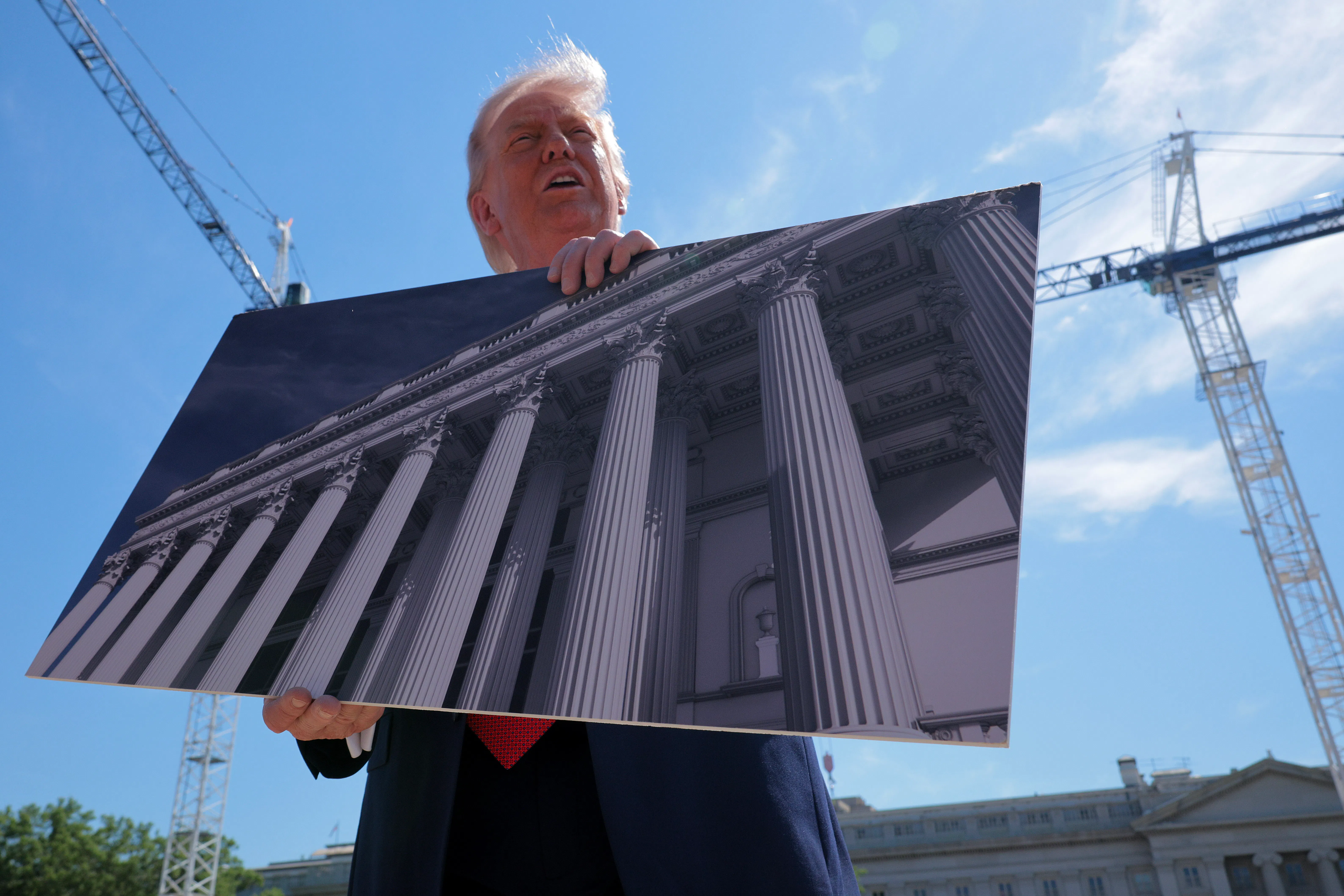 Donald Trump holds artists renderings as he talks to reporters about his proposed White House ballroom.