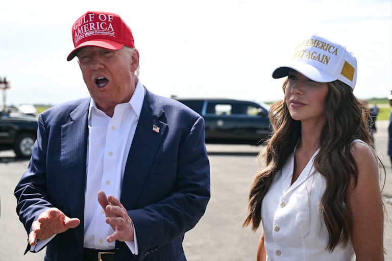 Donald Trump speaks and gestures while standing next to Kristi Noem on an airport tarmac