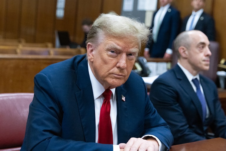 Donald Trump sits at a table, looking at the camera