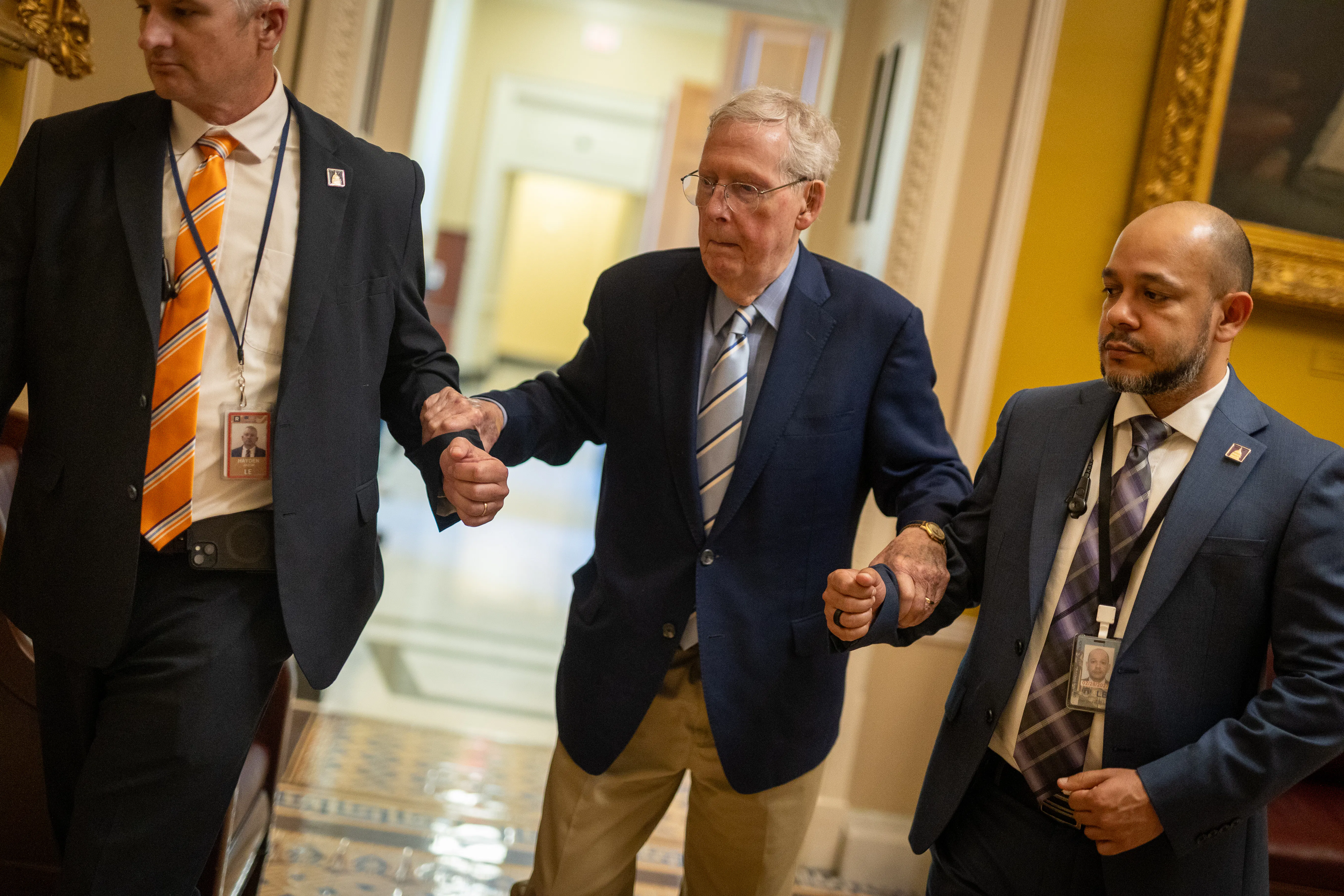 Senator Mitch McConnell is supported by two staffers as he walks in the Capitol