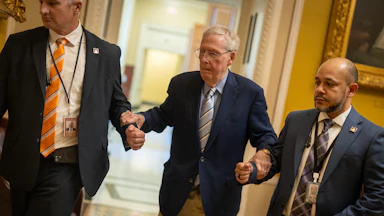 Senator Mitch McConnell is supported by two staffers as he walks in the Capitol