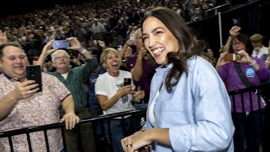 Representative Alexandria Ocasio-Cortez laughs as a crowd takes photos of her and smiles.