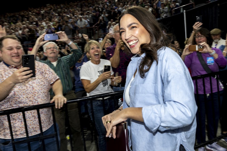 Representative Alexandria Ocasio-Cortez laughs as a crowd takes photos of her and smiles.