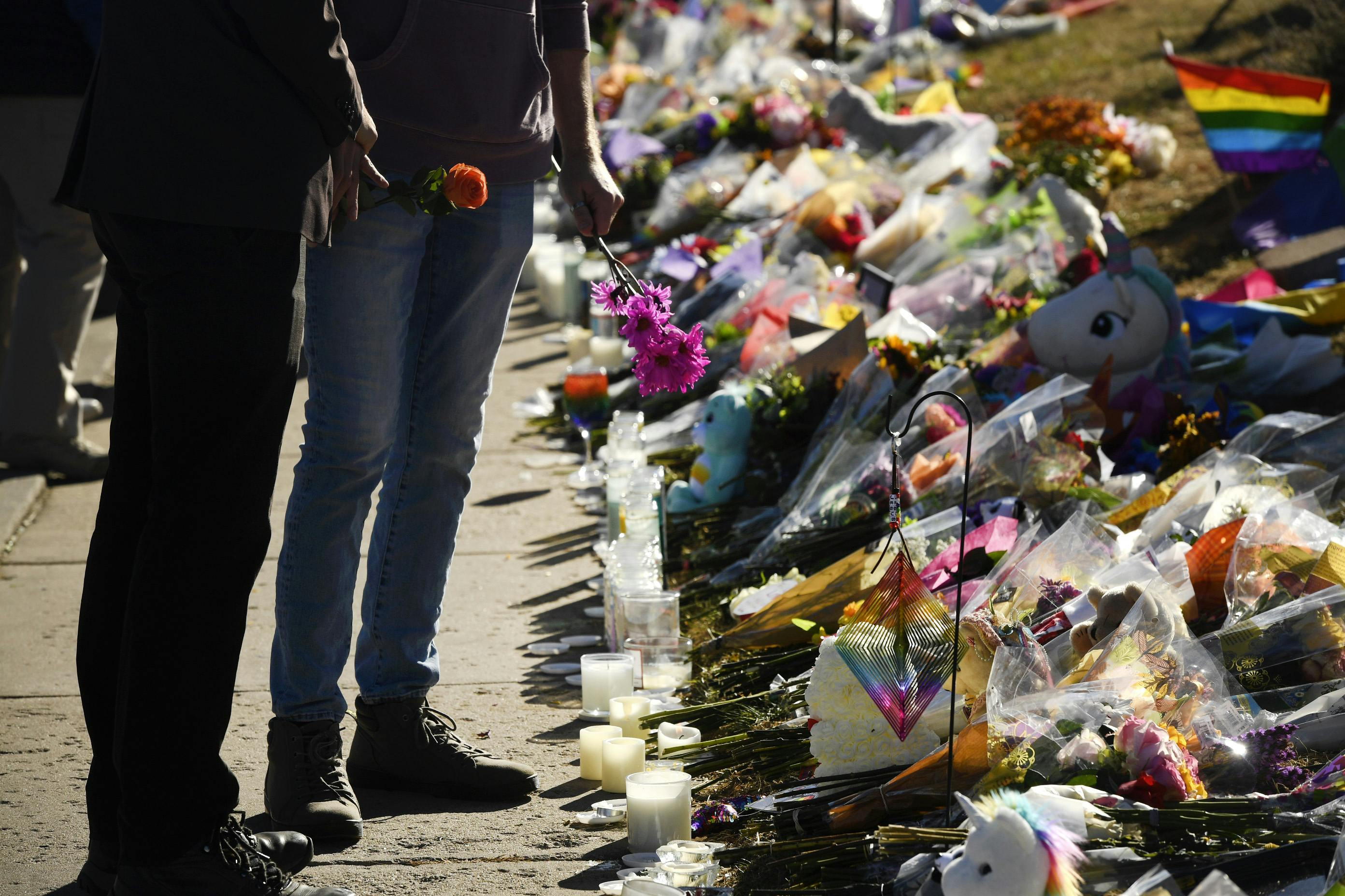Two people stand holding flowers in front of a pile of flowers and candles.
