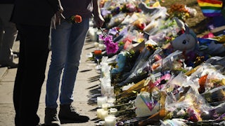 Two people stand holding flowers in front of a pile of flowers and candles.