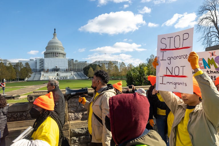 Protesters march outside the Capitol. One holds a sign that reads "Stop Ignorance, not Immigrants."