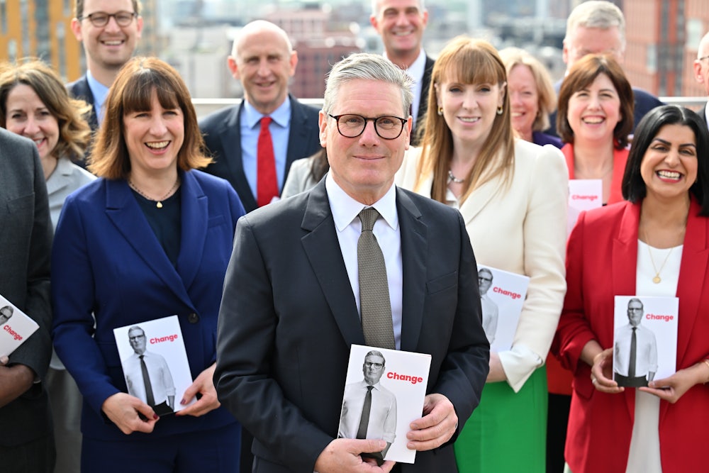 Keir Starmer poses holding a placard featuring his face and the word "change." Surrounding him are several other Labour officials holding the same placard.