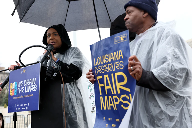 Black Louisiana voters and civil rights advocates call speak and hold signs that read "Louisiana Deserves Fair Maps" and "We Draw the Lines."