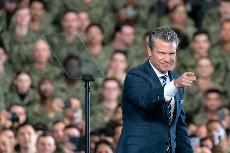 Defense Secretary Pete Hegseth points while standing onstage in front of troops on the USS George Washington