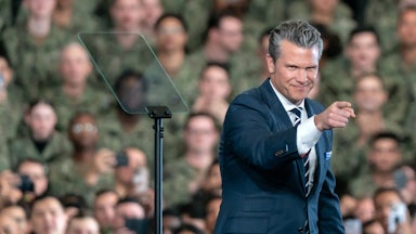 Defense Secretary Pete Hegseth points while standing onstage in front of troops on the USS George Washington