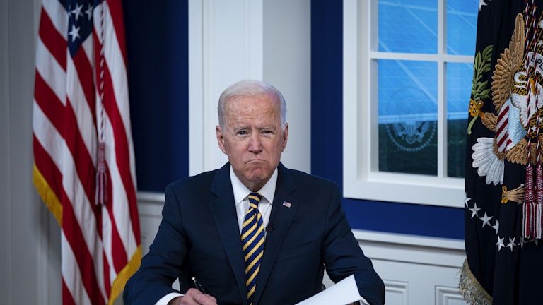 President Joe Biden grimaces as he signs some papers.
