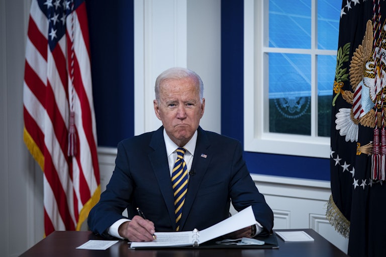 President Joe Biden grimaces as he signs some papers.