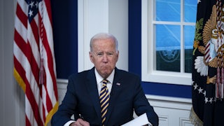 President Joe Biden grimaces as he signs some papers.
