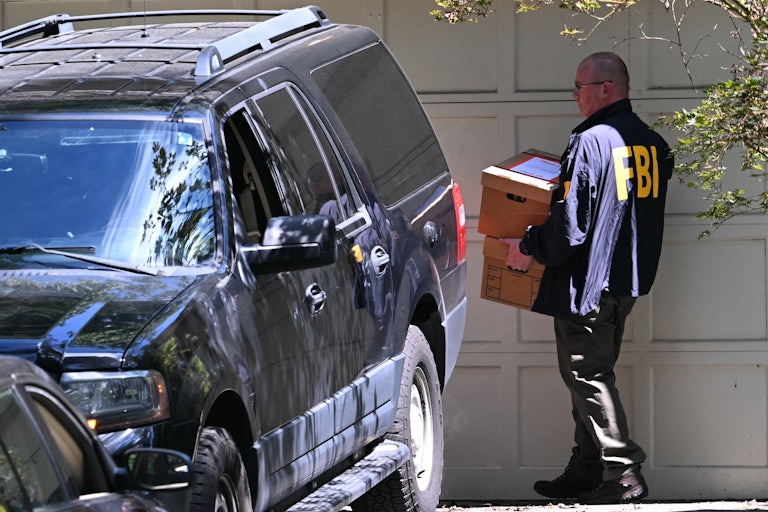 An FBI agent carries a box outside former national security advisor John Bolton’s house in Maryland.
