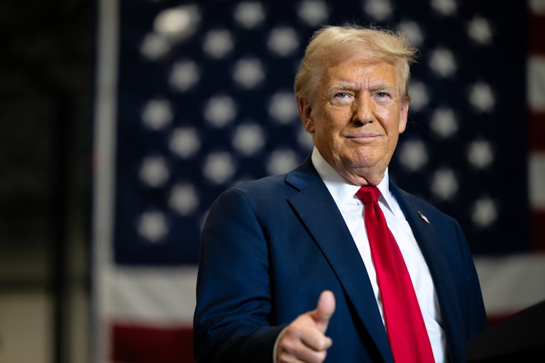 Donald Trump smiles and gives a thumbs up. He looks very old and his makeup looks very patchy.