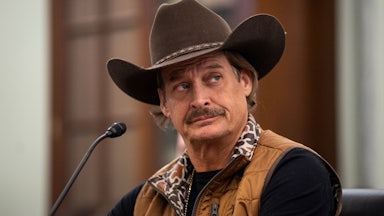 Kid Rock looks to the side while sitting at a microphone in a congressional hearing