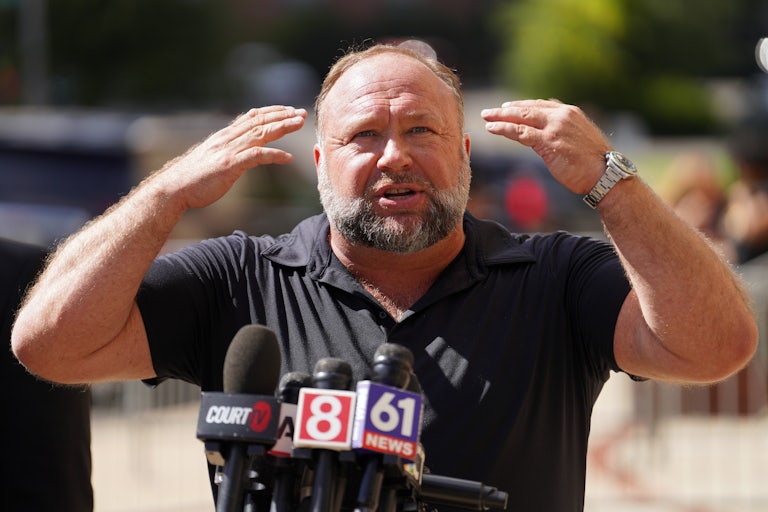 Alex Jones puts both hands toward his head as he speaks at a press conference.