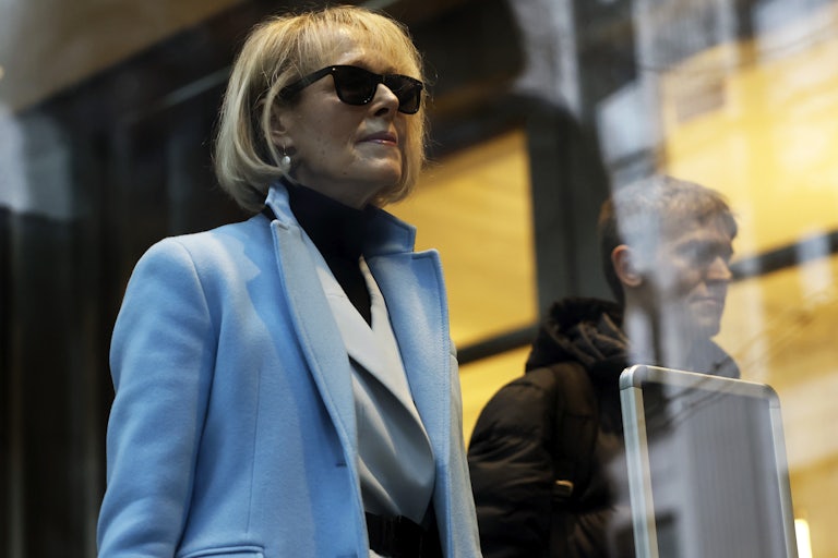 E. Jean Carroll stands wearing a blue coat and black sunglasses