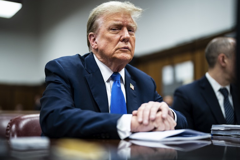 Donald Trump looks down as he sits with his hands folded
