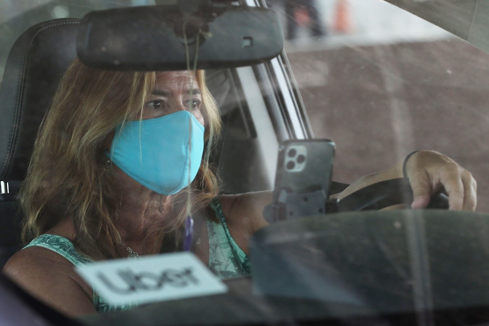 A white woman wearing a light blue cloth mask drives an Uber