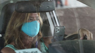 A white woman wearing a light blue cloth mask drives an Uber
