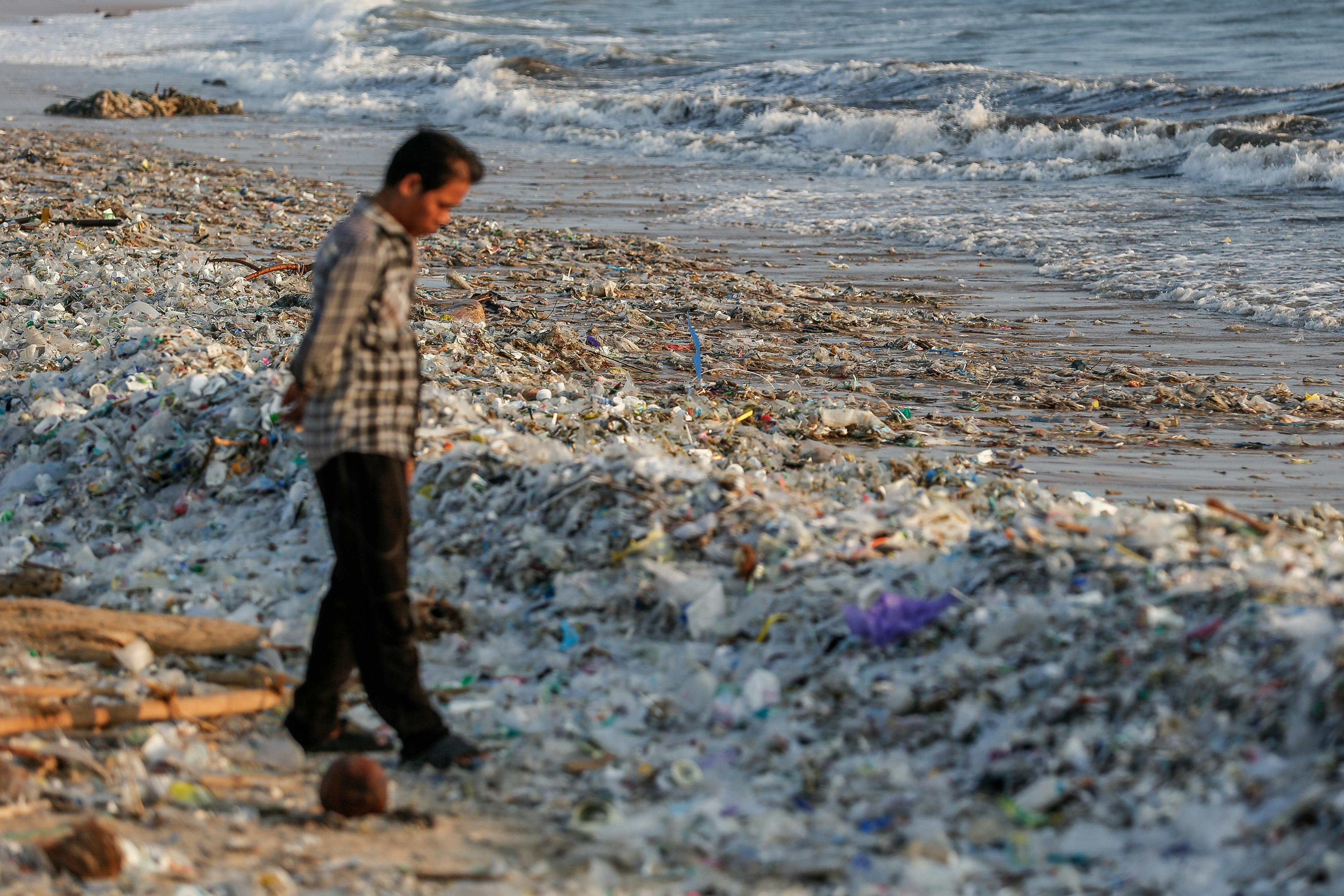 A man stands on a beach with mounds of plastic at his feet.