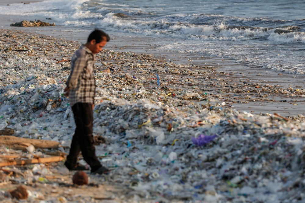 A man stands on a beach with mounds of plastic at his feet.