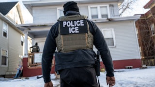 An ICE agent heads to a house, the yard blanketed in snow.