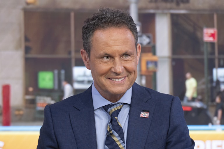 Fox News host Brian Kilmeade smiles while sitting on the set of Fox & Friends