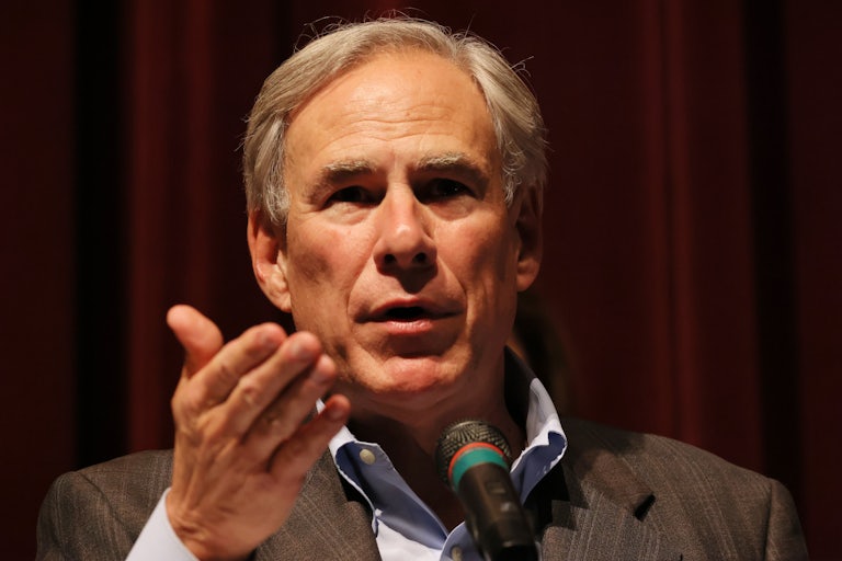 Greg Abbott speaks in front of a mic with hand outraised
