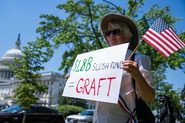 A woman outside the Capitol holds up a sign that reads "$1.8B Slush Fund = GRAFT"