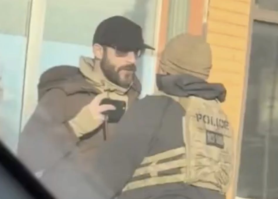 Screenshot of a video where Alex Pretti holds a phone near his chest, recording, as a Border Patrol agent gets in his face.