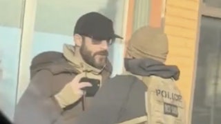 Screenshot of a video where Alex Pretti holds a phone near his chest, recording, as a Border Patrol agent gets in his face.
