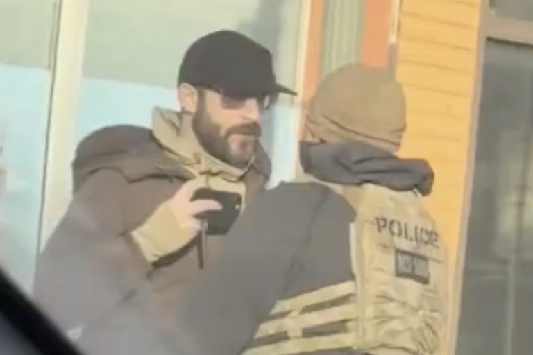 Screenshot of a video where Alex Pretti holds a phone near his chest, recording, as a Border Patrol agent gets in his face.