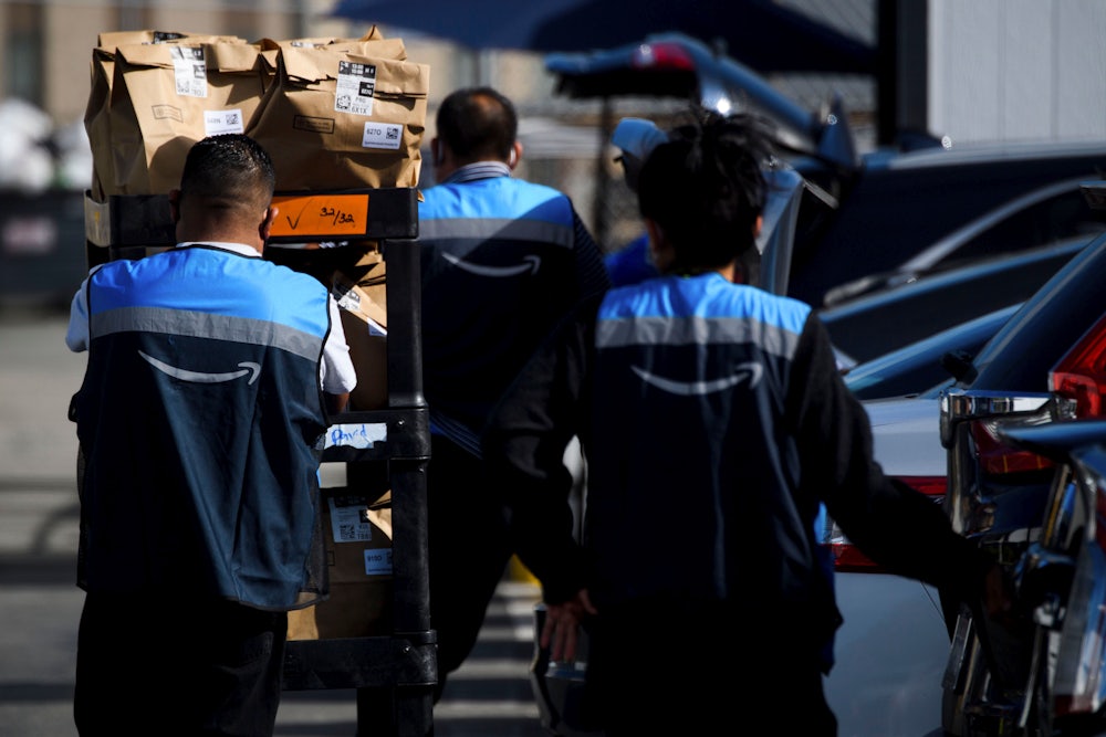 An Amazon delivery driver scans bags of groceries while loading a vehicle outside of a distribution facility