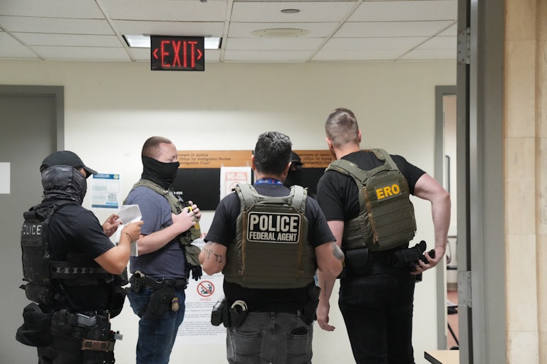 Four men wearing face masks and police vests stand inside a building.