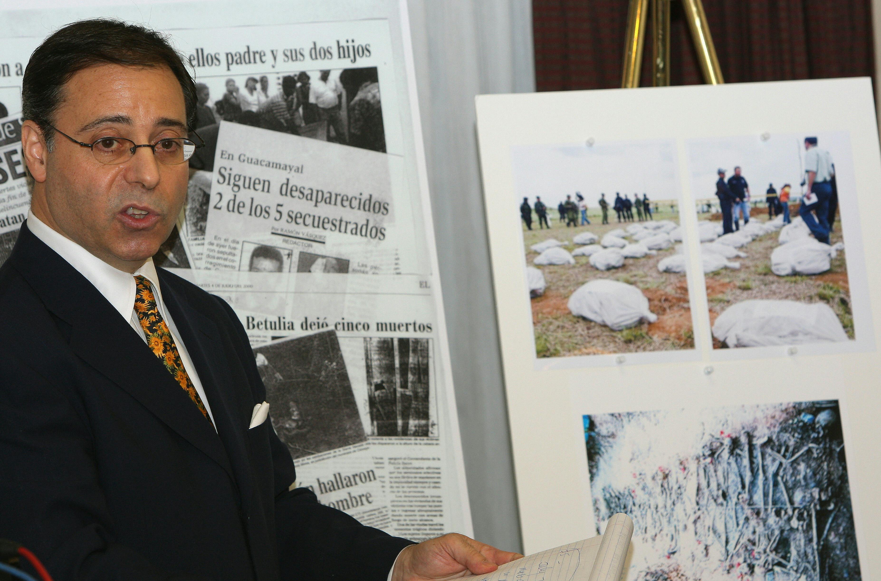 A man stands in front of newspaper clippings and photographs.