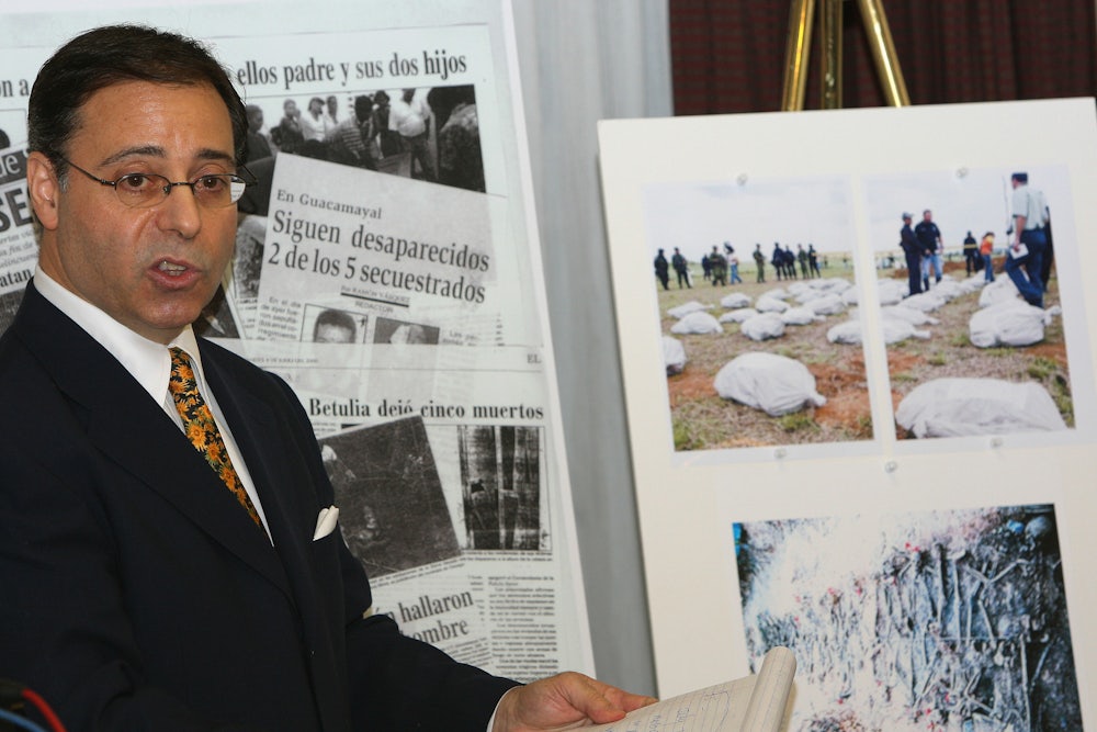 A man stands in front of newspaper clippings and photographs.