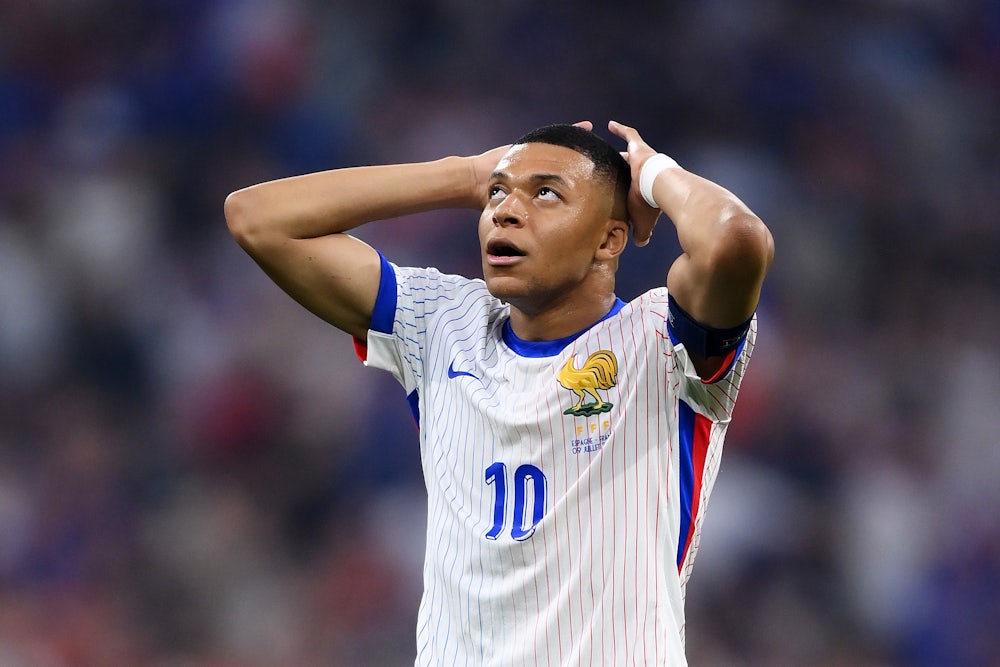 Kylian Mbappe looks up at the sky, arms on his head, in shock.
