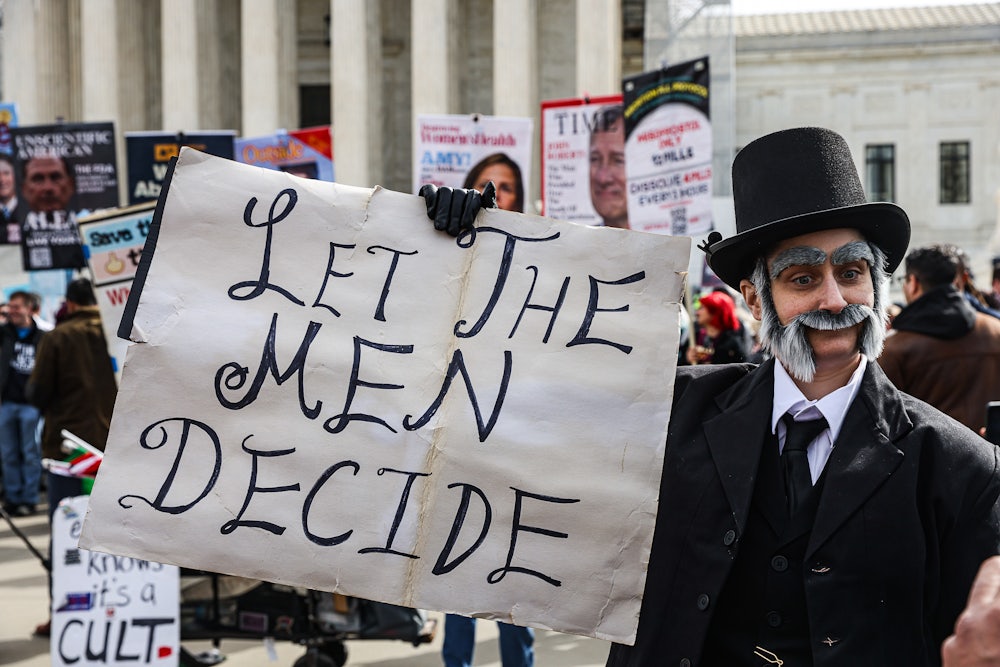A demonstrator in historical costume holds a sign reading "let the men decide"