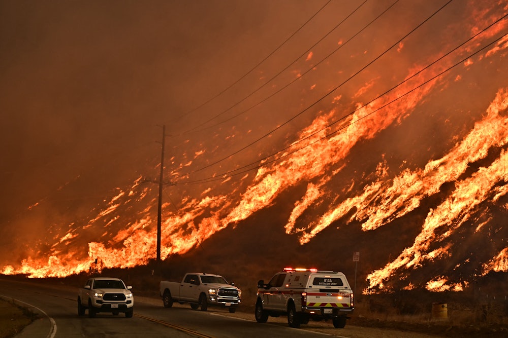 Emergency vehicles stand on the road in front of a hill on fire.
