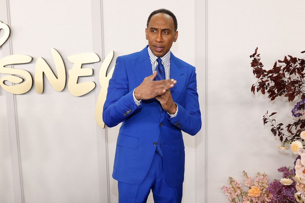 stephen a. smith wears a blue suit and does a time out gesture while standing in front of a large disney logo